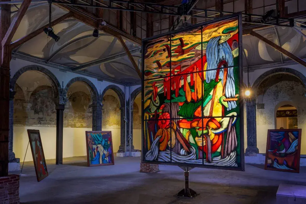 Vetrate colorate e quadri astratti in una galleria d'arte, con un'opera di ara starck al centro.