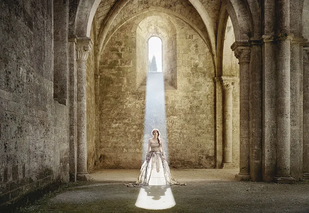 Cristina Vatielli, vestita di bianco, in piedi sotto un raggio di luce in un'antica abbazia.