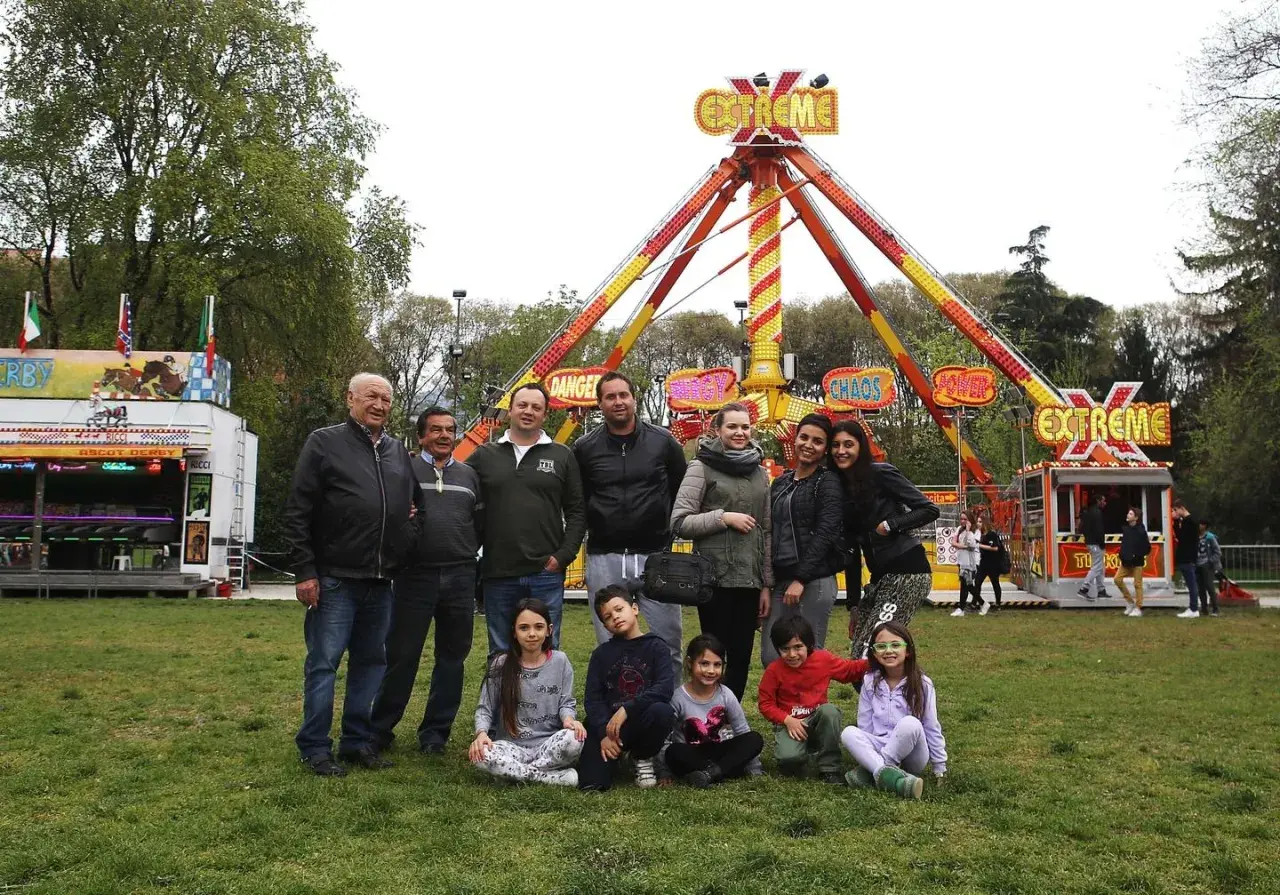 Famiglie giostrai italiani posano sorridenti davanti a un'attrazione "Extreme" in un parco divertimenti.
