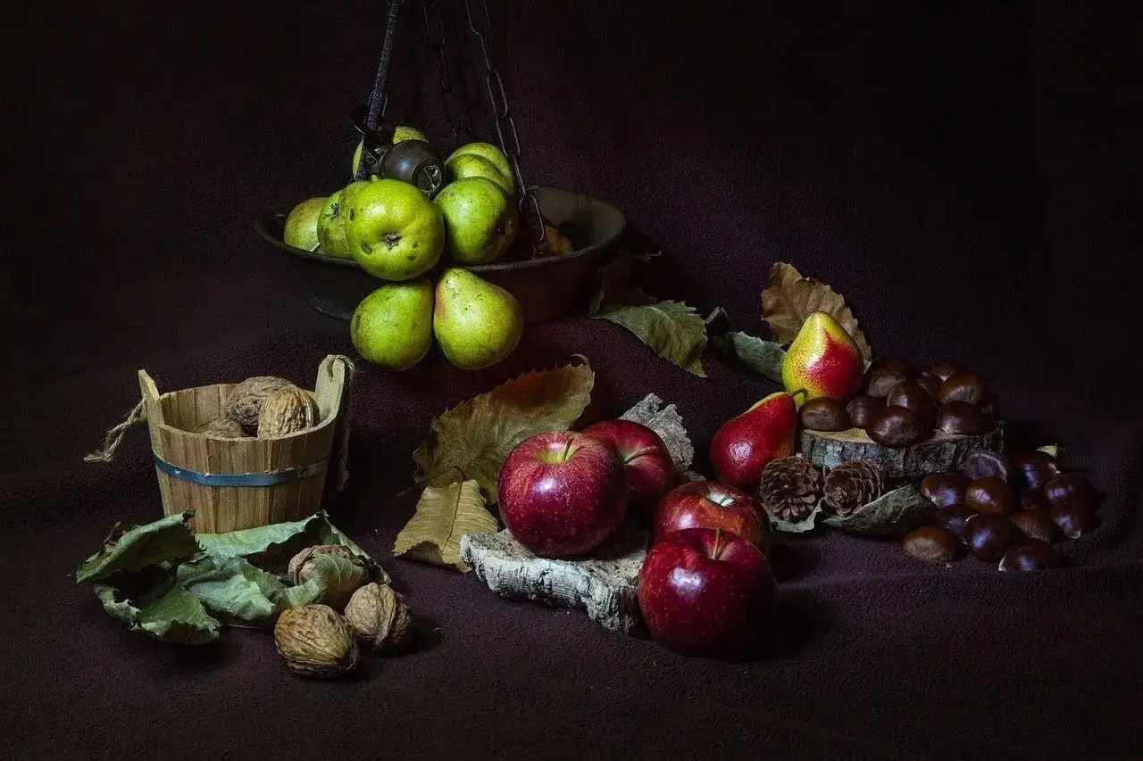 Esempi still life fotografia: mele rosse, pere verdi e rosse, noci in un cesto di legno e castagne su un tronco.