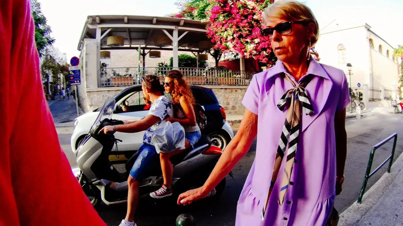 Donna in viola con foulard a quadri, mentre una coppia su scooter passa. Scatto con ace pro 2.