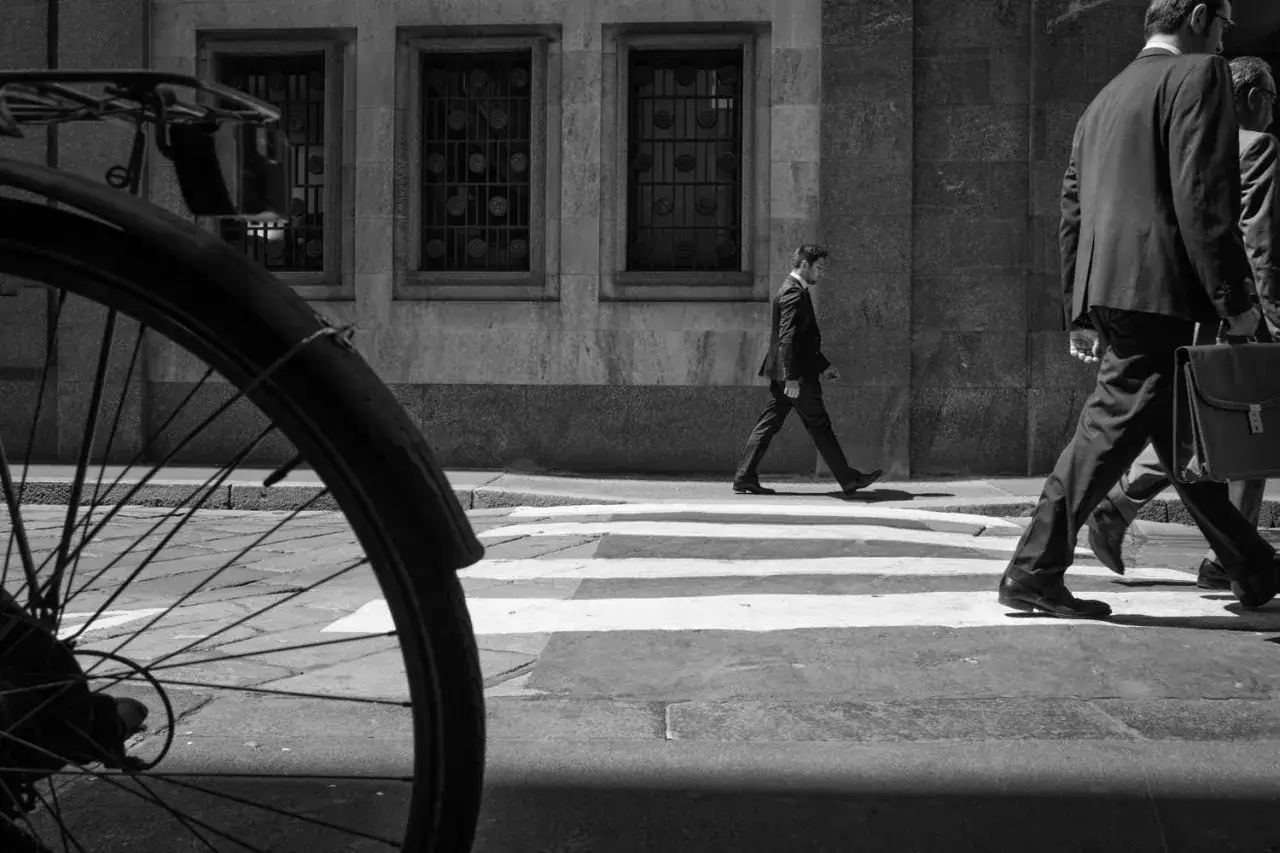 Uomo in giacca e cravatta attraversa la strada, un'immagine che cattura il leica significato di un momento urbano.