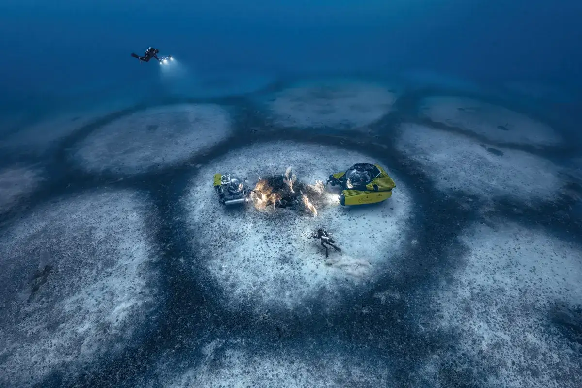 Laurent Ballesta esplora il fondale marino con mini sottomarini gialli e subacquei, illuminando misteriosi cerchi sul fondale.